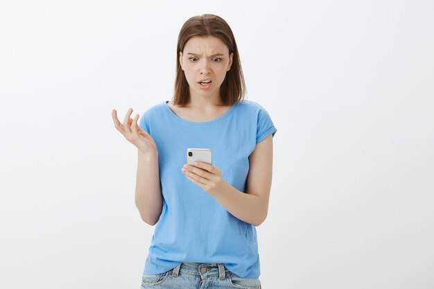 Расстроенная и обеспокоенная женщина, смотрящая на экран смартфона, смущена