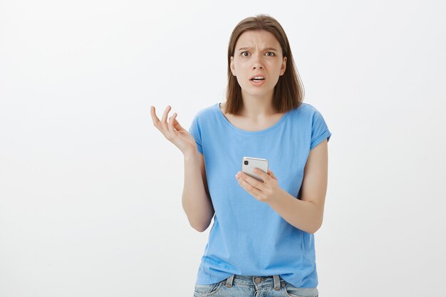 Frustrated and bothered woman looking at smartphone screen confused