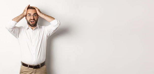 Frustrated businessman holding hands on head looking shocked and anxious standing over white backgro