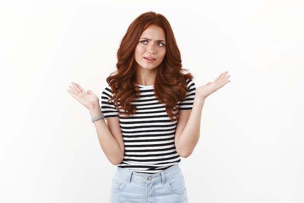 Frustrated and confused cute modern redhead young girl in striped tshirt looking puzzled frowning troubled and unsure shrugging hands raised up dismay staring sideways uncertain