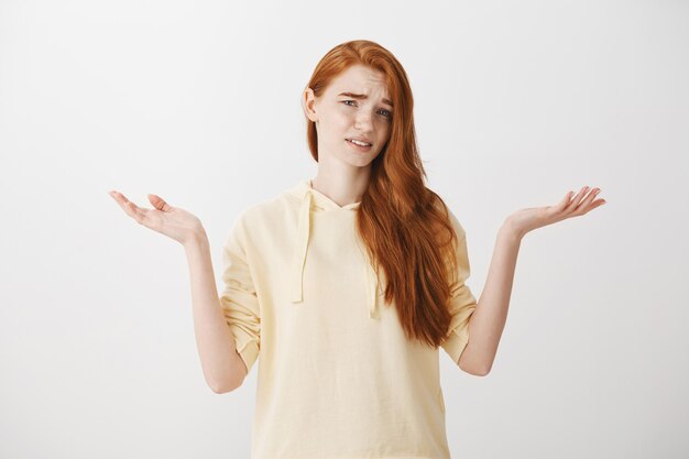 Frustrated and confused redhead girl shrugging with displeased look