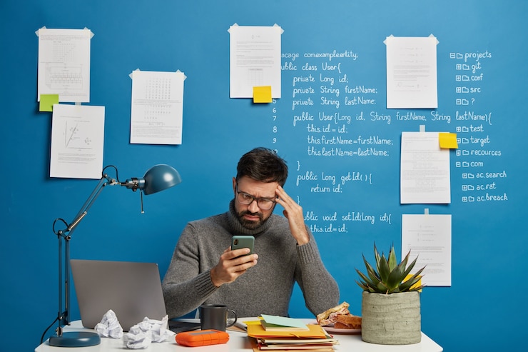 Free Photo frustrated depressed male freelancer cannot send message to client, looks sadly at smartphone, keeps hand on temple, suffers from headache