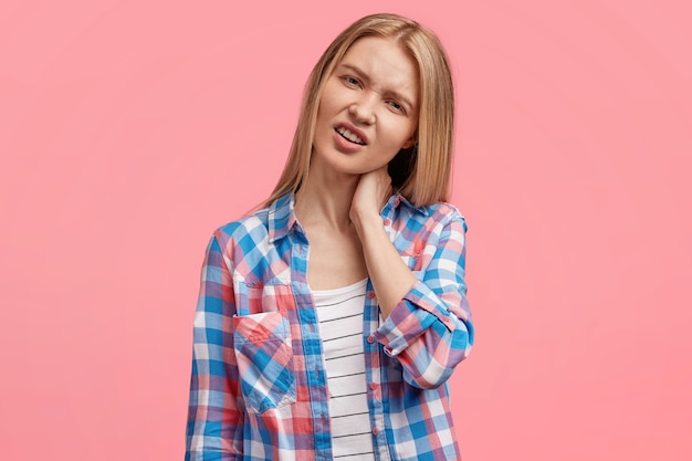 Frustrated displeased blonde young cute female has strong pain in neck