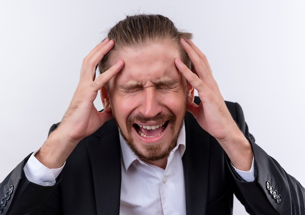 Frustrated handsome business man wearing suit holding his head with hands standing over white background