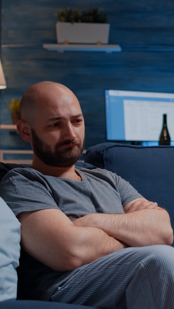 Frustrated man staring in space sitting alone on sofa feeling depressed