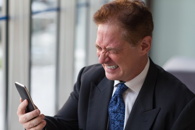 Frustrated senior manager holding mobile phone