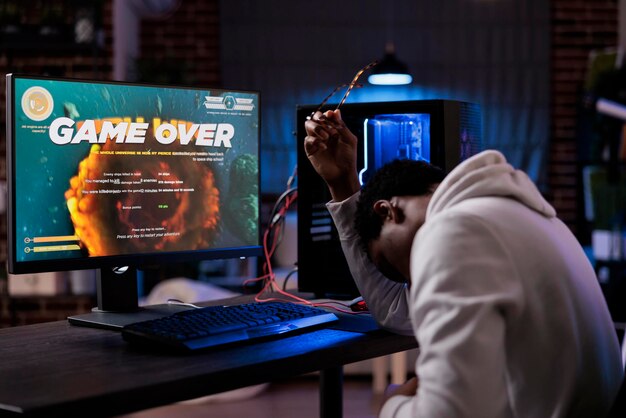 Frustrated streamer losing online shooter video games play competition on computer with neon lights. Male gamer streaming action gameplay and feeling sad about lost shooting championship.