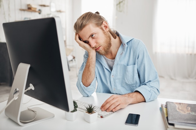 イライラした疲れたあごひげを生やしたコーカサス地方の従業員が頭に触れ、過労、計算の計算、コンピューター画面の前に座っているために完全に疲れきっています。締め切りと過労