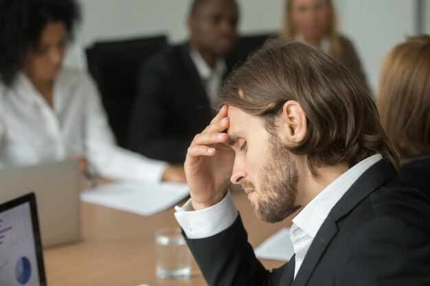 Frustrated tired businessman having strong headache at diverse team meeting