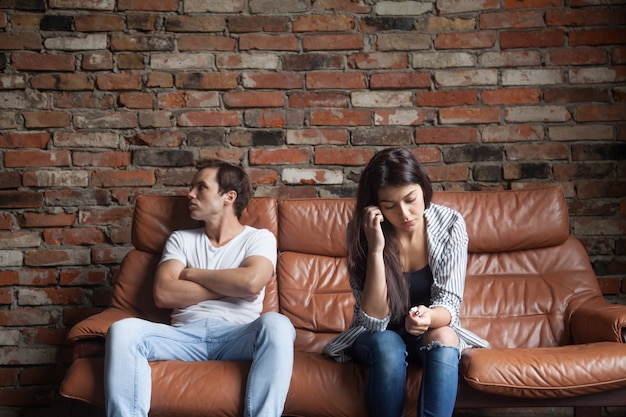 Frustrated upset couple after quarrel sitting on sofa at home