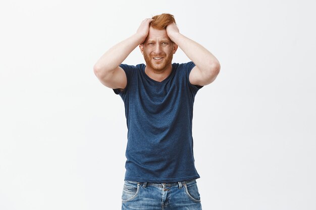 Free photo frustrated upset redhead euroepan man in trouble, holding hands on head, frowning and grimacing from sadness and grief