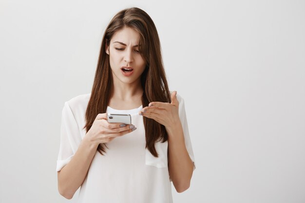 Frustrated woman complaining at something, pointing bothered at mobile phone display