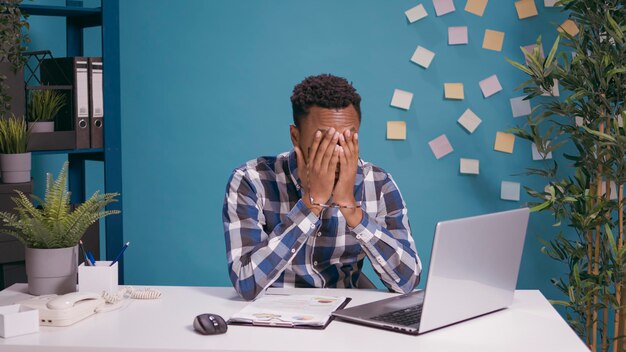 Frustrated worker feeling exhausted about office work, using laptop computer at desk. Tired employee working on business plan, feeling angry and disappointed about financial mistake.