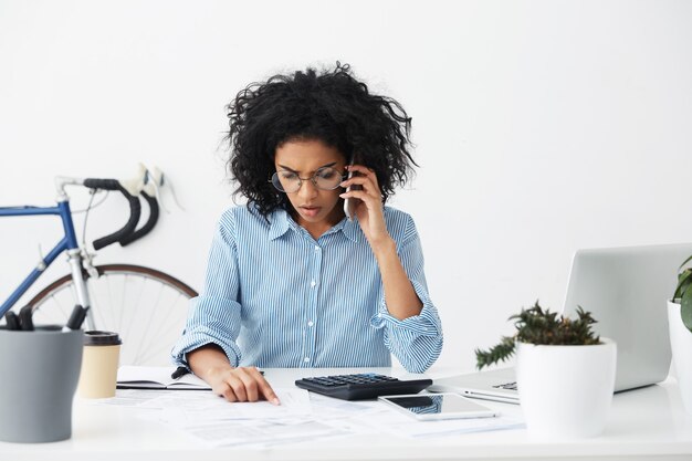 Frustrated young Afro American female accountant in stylish round eyeglasses