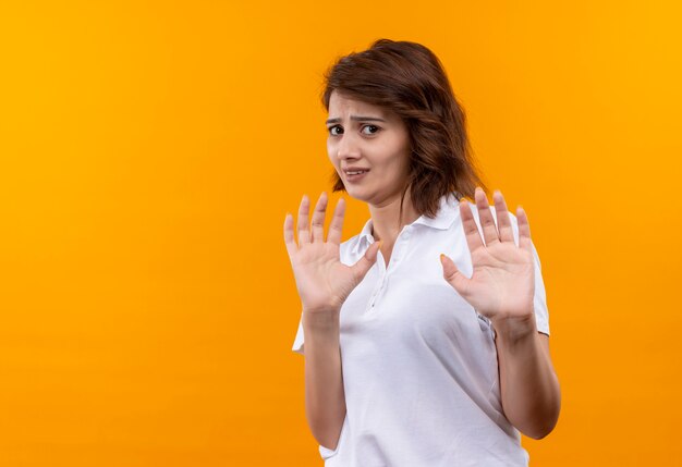 Frustrated young girl with short hair wearing white polo shirt making defense gesture with disgusted expression