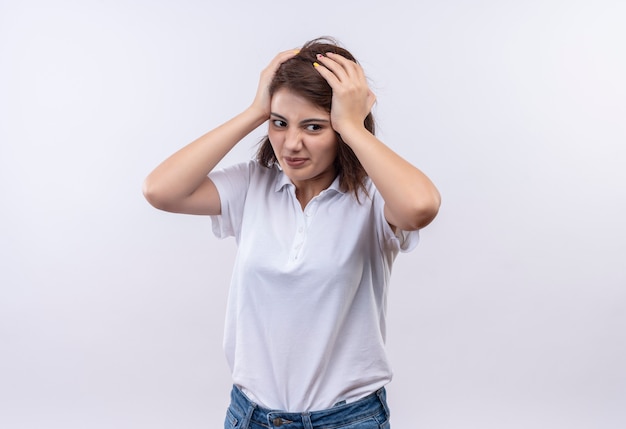 Frustrated young girl with short hair wearing white polo shirt touching head very angry 