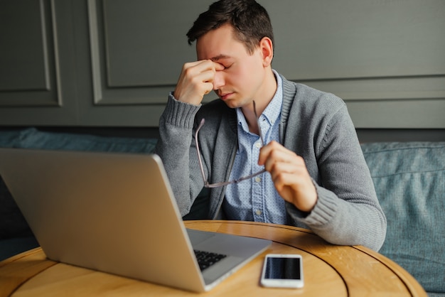 Free photo frustrated young man massaging his nose and keeping eyes closed while working