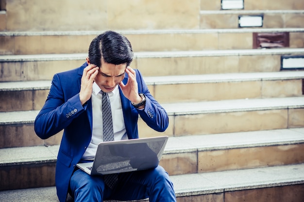 Frustrated young man sitting on staircase working with laptop. Unhappy problem with work.