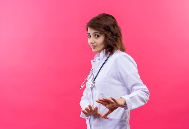 Разочарованная молодая женщина-врач в белом халате со стетоскопом делает защитный жест с выражением отвращения
