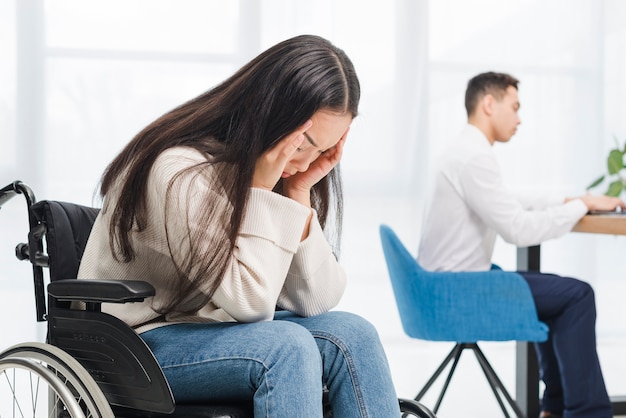 사무실에서 일하는 사업가의 앞에 휠체어에 앉아 두통으로 고통 좌절 젊은 여자