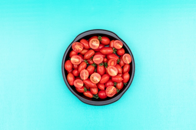 The fry pan filled with cherry tomatoes in center on light blue surface