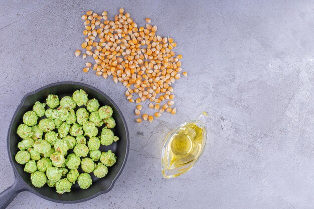 Frying pan containing popcorn candy accompanied by ingredients to make popcorn on marble background. High quality photo