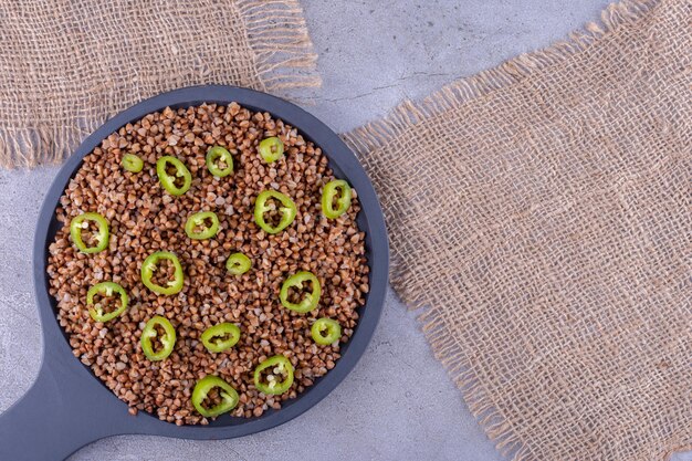 Frying pan full of cooked buckwheat with pepper slice topping on marble background. High quality photo