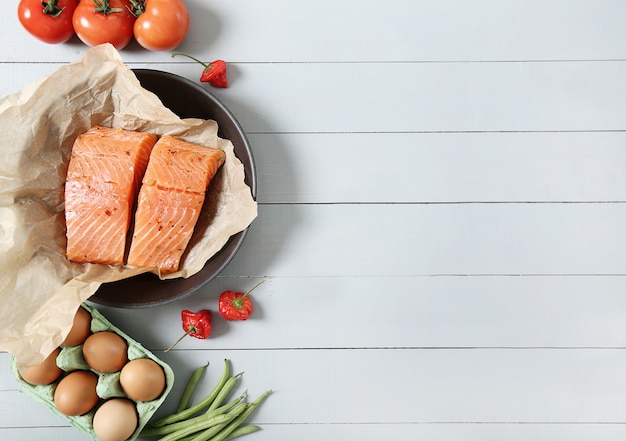 Free photo frying pan with raw salmon, tomatoes and eggs on wooden background