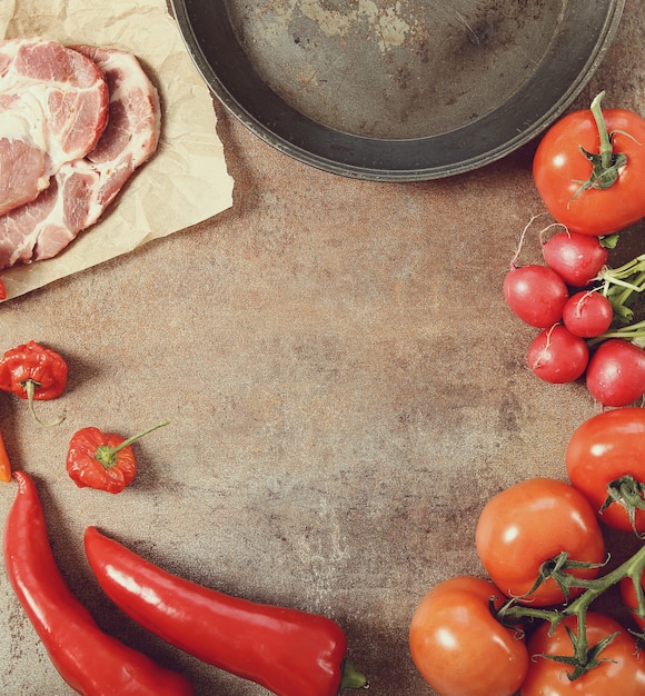 frying pan with vegetables and raw meat, top view background