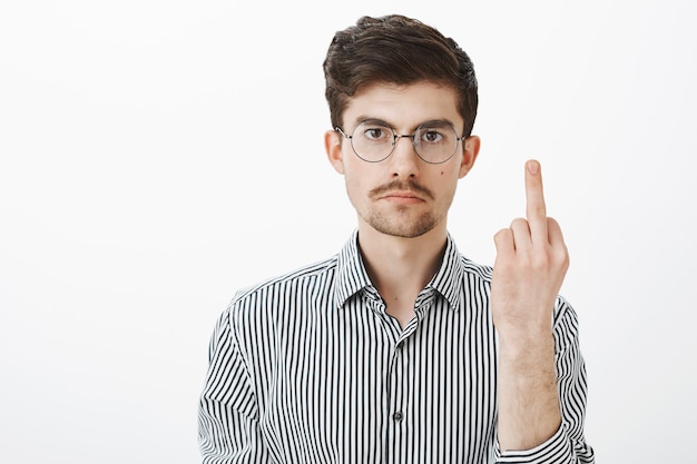 Free photo fuck off, man, i am not your slave. annoyed serious adult male with bristle and moustache, showing middle finger and staring with calm expression, being fed up of mocking over gray wall