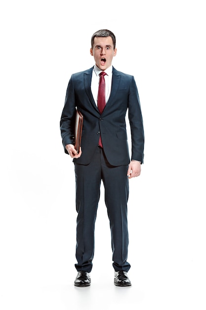 Полное тело или портрет бизнесмена или дипломата с папкой на белой предпосылке студии. Удивленный молодой человек в костюме, красный галстук, стоя в офисе. Бизнес, карьера, концепция успеха.