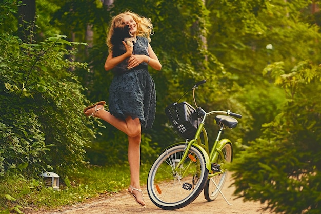 ブロンドの女の子の全身画像は、自転車の背景の上にスピッツ犬を保持しています。
