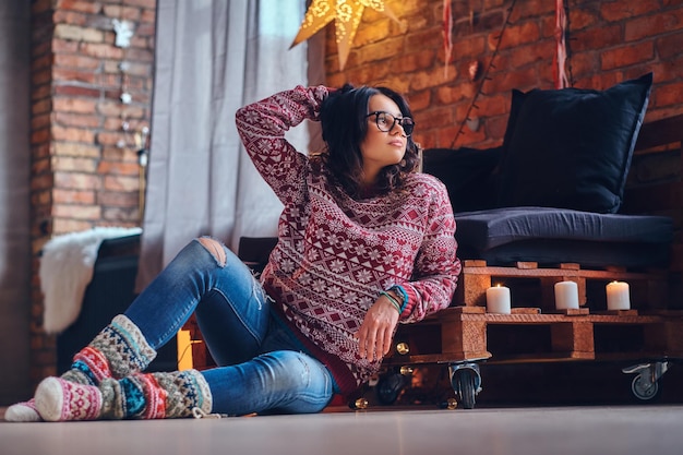 Full body image of sexy brunette femalesits on a floor in a room with Christmas decoration.