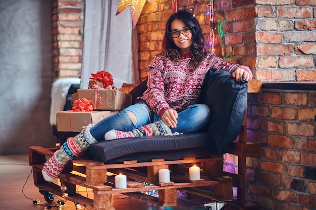 Full body image of sexy brunette femalesits on a floor in a room with Christmas decoration.