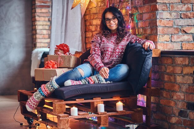 Full body image of sexy brunette femalesits on a floor in a room with Christmas decoration.