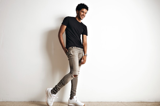 Full body portrait of a cute tall young african american model with an afro in a plain black cotton t-shirt, white sneakers and slim grey jeans isolated on white