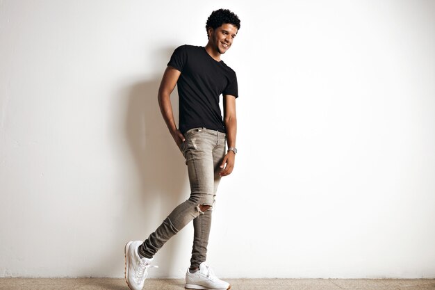 Full body portrait of a cute tall young African American model with an afro in a plain black cotton t-shirt, white sneakers and slim grey jeans isolated on white