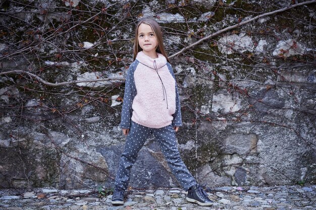 灰色の岩の背景に暖かい秋の服を着た少女の全身の肖像画。