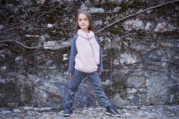 회색 바위 배경에 따뜻한 가을 옷을 입은 어린 소녀의 전신 초상화.