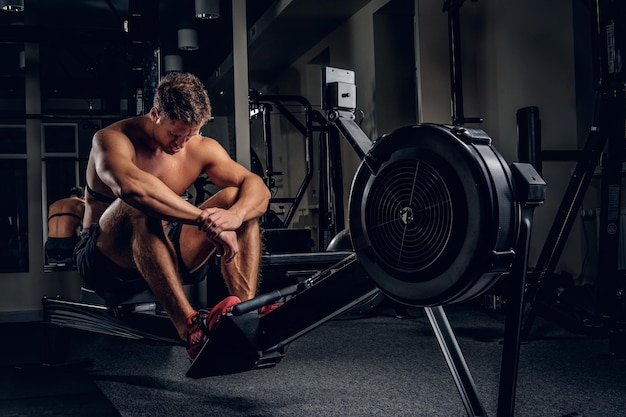 Ritratto completo del corpo di un maschio sportivo stanco dopo gli allenamenti su una macchina per esercizi di potenza in una palestra.