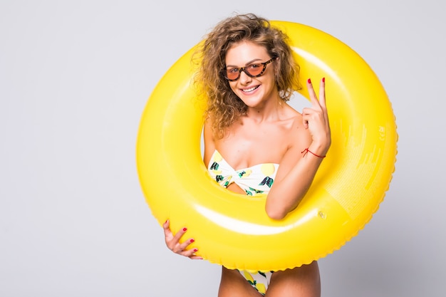 Full body sexy woman in bikini with yellow inflatable ring isolated over white wall