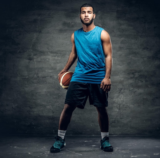 Ritratto in studio per tutto il corpo di un giocatore di basket nero che gioca con una palla.