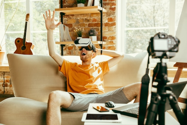 감정이 가득합니다. 집에서 VR 안경의 비디오 리뷰를 녹화하는 전문 카메라가있는 백인 남성 블로거