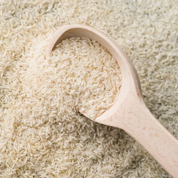 Full frame of white uncooked rice with wooden spoon