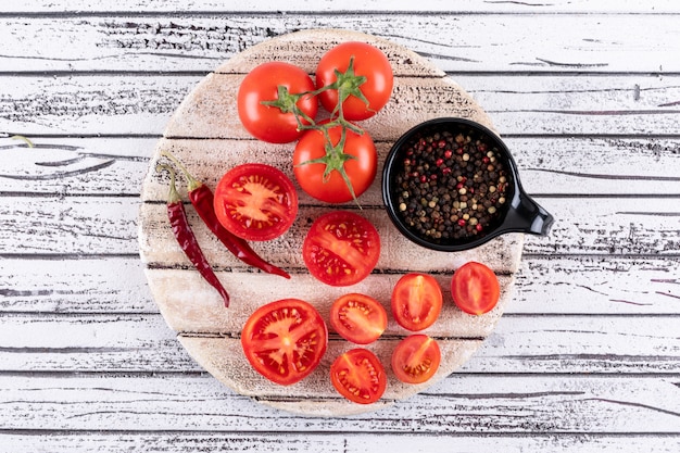 Full and half tomatoes on white board dry red hot chili pepper isolated and black pepper powder in black bowl on white wooden surface