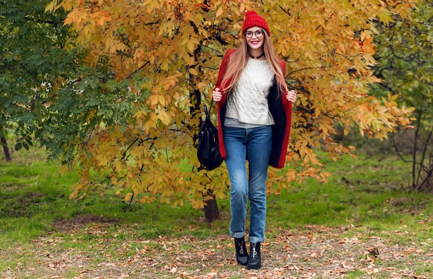 Full height autumn fashion image of pretty nice woman in red stylish coat and knitted hat, red lips posing on yellow park.