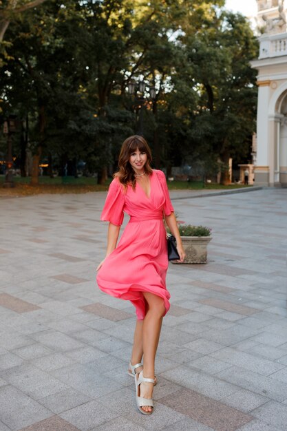Полное изображение довольно романтичной женщины в розовом платье, позирующем на открытом воздухе в старой Европе.