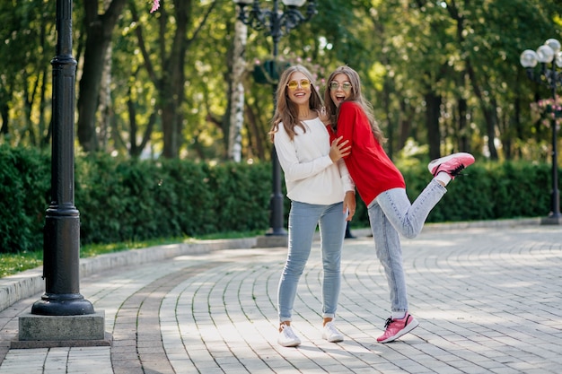 Full-lenght outdoor portrait of two pretty friendly happy girls having fun and walking together after study in the city, sunny day, good true emotions, funny mood