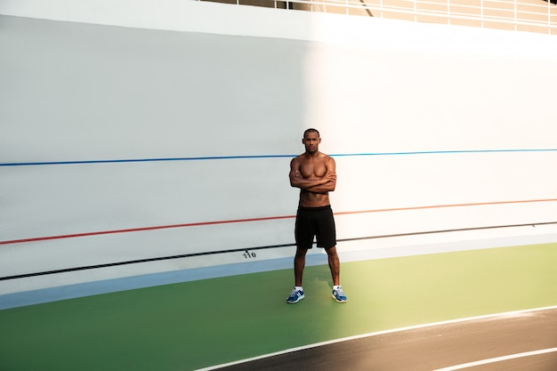 Full-lenght photo of young african sports man, standing with crossed hands