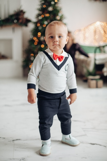 Full lenght portrait of a trendy toddler with red bow standing in living room decorated for Christmas